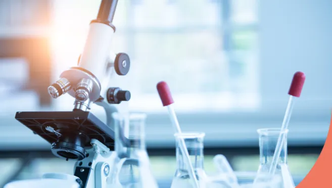 A microscope on a table, surrounded by chemical glass equipment in front of a window with a Coveris logo in the right bottom corner